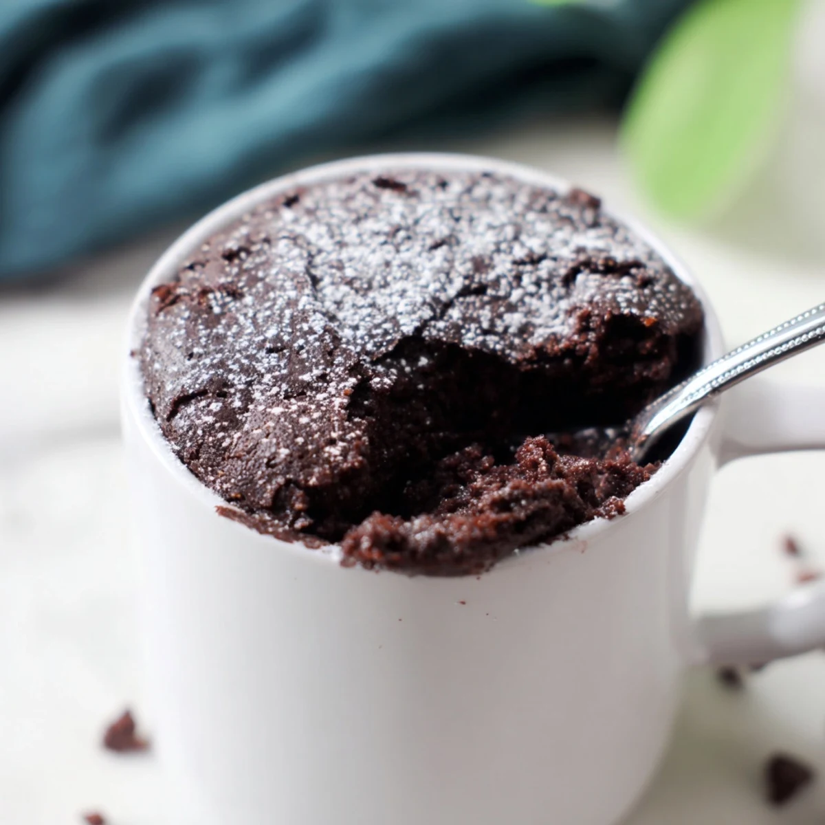 A close-up of a chocolate microwave mug cake, served warm in its wide ceramic mug.