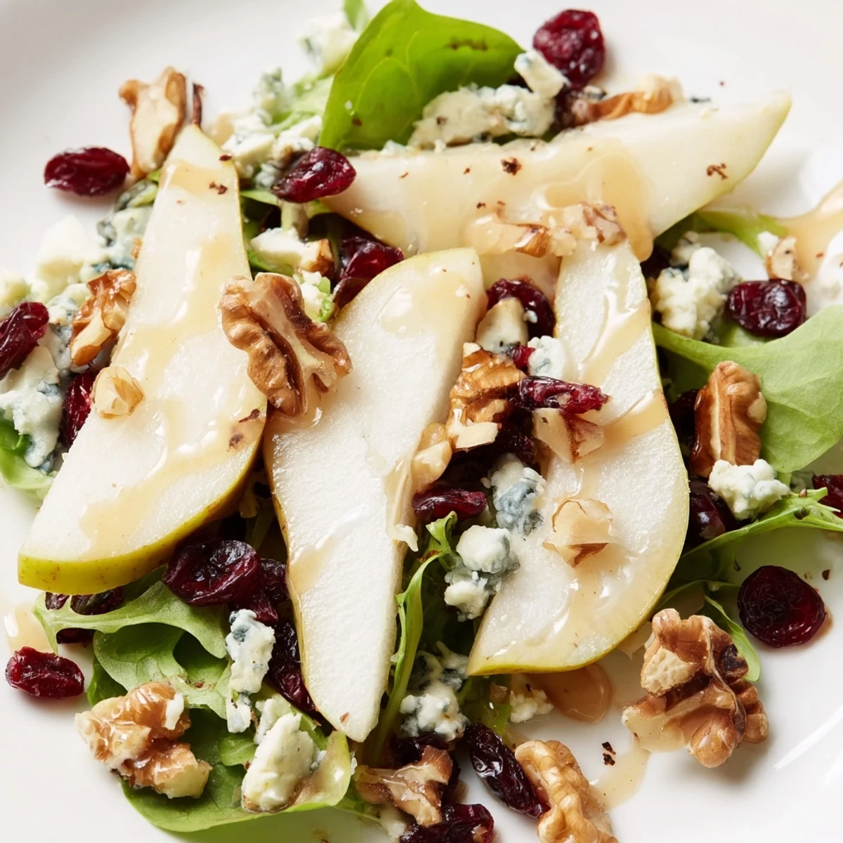 A close-up of vibrant pear Gorgonzola salad with mixed greens, crumbled cheese, and toasted walnuts on a rustic wooden table.  