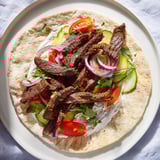 Warm flatbread wraps filled with flavorful beef shawarma, drizzled with creamy yogurt sauce.