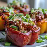 A close-up of baked Korean-Style Turkey Stuffed Sweet Peppers on a rustic board, garnished with sesame seeds and fresh green onions, served warm.