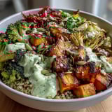 A colorful vegan Buddha bowl filled with roasted sweet potato, broccoli, and bell pepper, topped with creamy green goddess avocado dressing.  