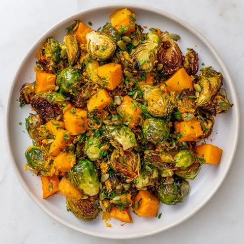 Golden-brown Roasted Brussels Sprouts & Butternut Squash, drizzled with vibrant orange dressing and herbs.
