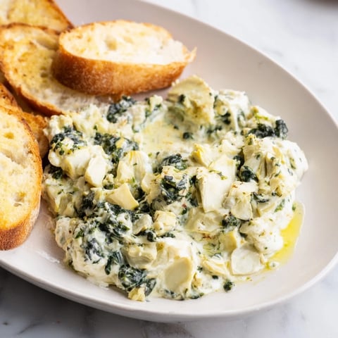 Warm, bubbly Spinach Artichoke Dip served with golden toasted baguette slices, perfect for sharing.