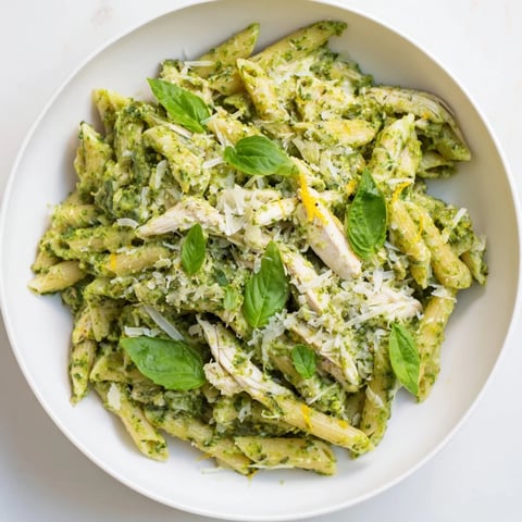 Steaming bowl of 10-Minute Pesto Pasta with Chicken, garnished with fresh basil and Parmesan cheese.
