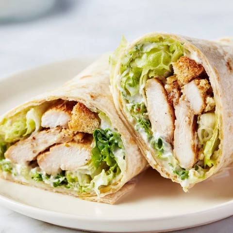 Grilled chicken slices rest atop a Caesar salad in a soft tortilla wrap, ready to eat.