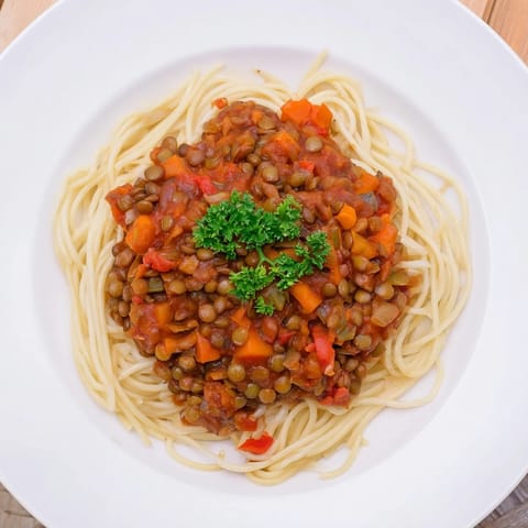 A steaming bowl of Hearty Lentil Bolognese, thick tomato sauce over perfectly cooked pasta, ready to eat.