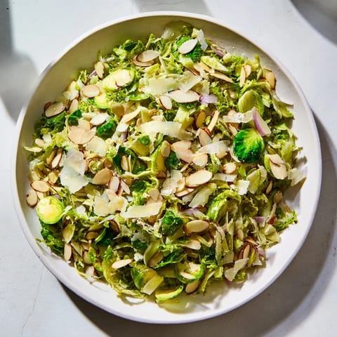 Fresh, vibrant photo of Crunchy Lemon Parmesan Brussels Sprouts Salad, topped with toasted almonds and cheese.