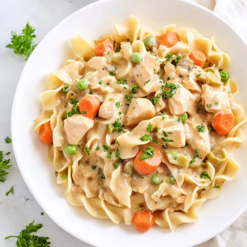 A close-up of a bowl of creamy Chicken and Egg Noodles, topped with fresh parsley.