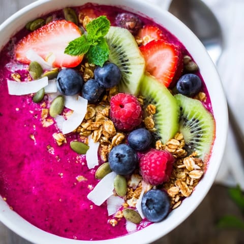 A creamy bowl of Beet and Berry Smoothie Bowl, swirled with almond milk yogurt and sprinkled with pumpkin seeds and coconut.  
