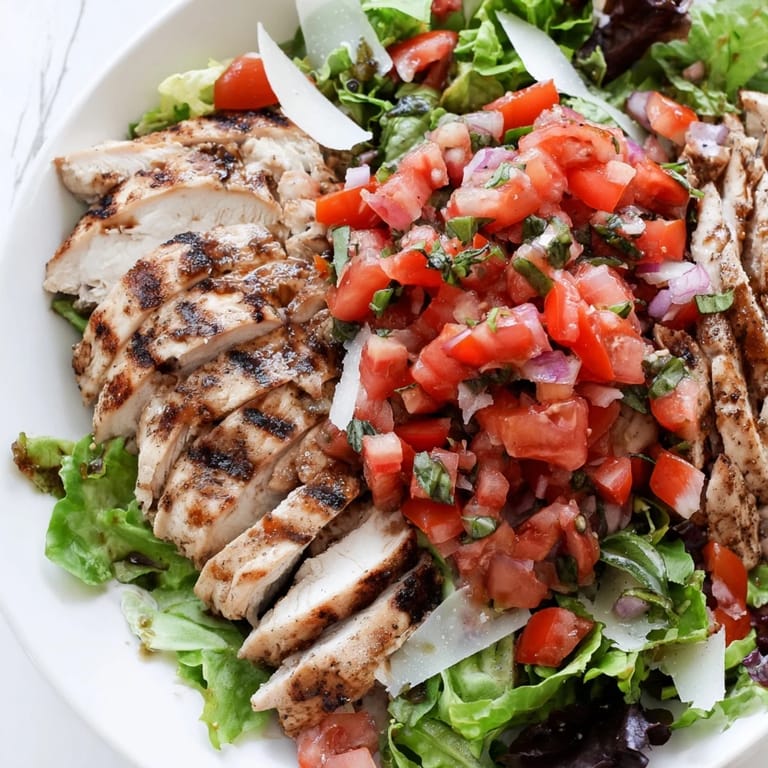 Savory Bruschetta Chicken Salad plated with lemon wedges, showcasing tender grilled chicken, balsamic tomatoes, and Parmesan over a fresh salad base.