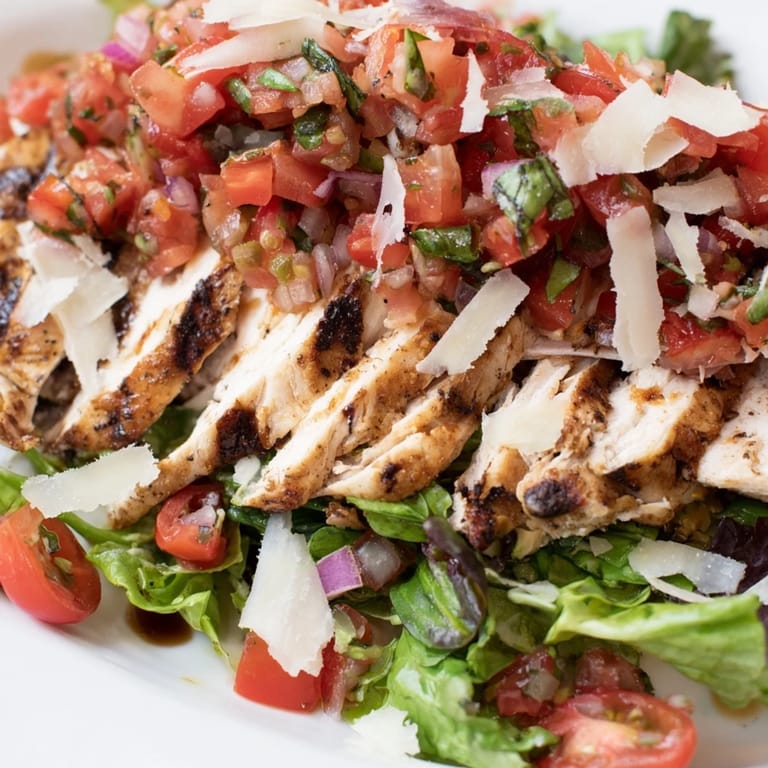 Bright and zesty Bruschetta Chicken Salad featuring juicy grilled chicken, diced tomatoes, fresh basil, and shaved Parmesan on a bed of greens.