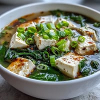 A warm bowl of miso soup with silken tofu, fresh spinach, and green onions in a savory broth.  